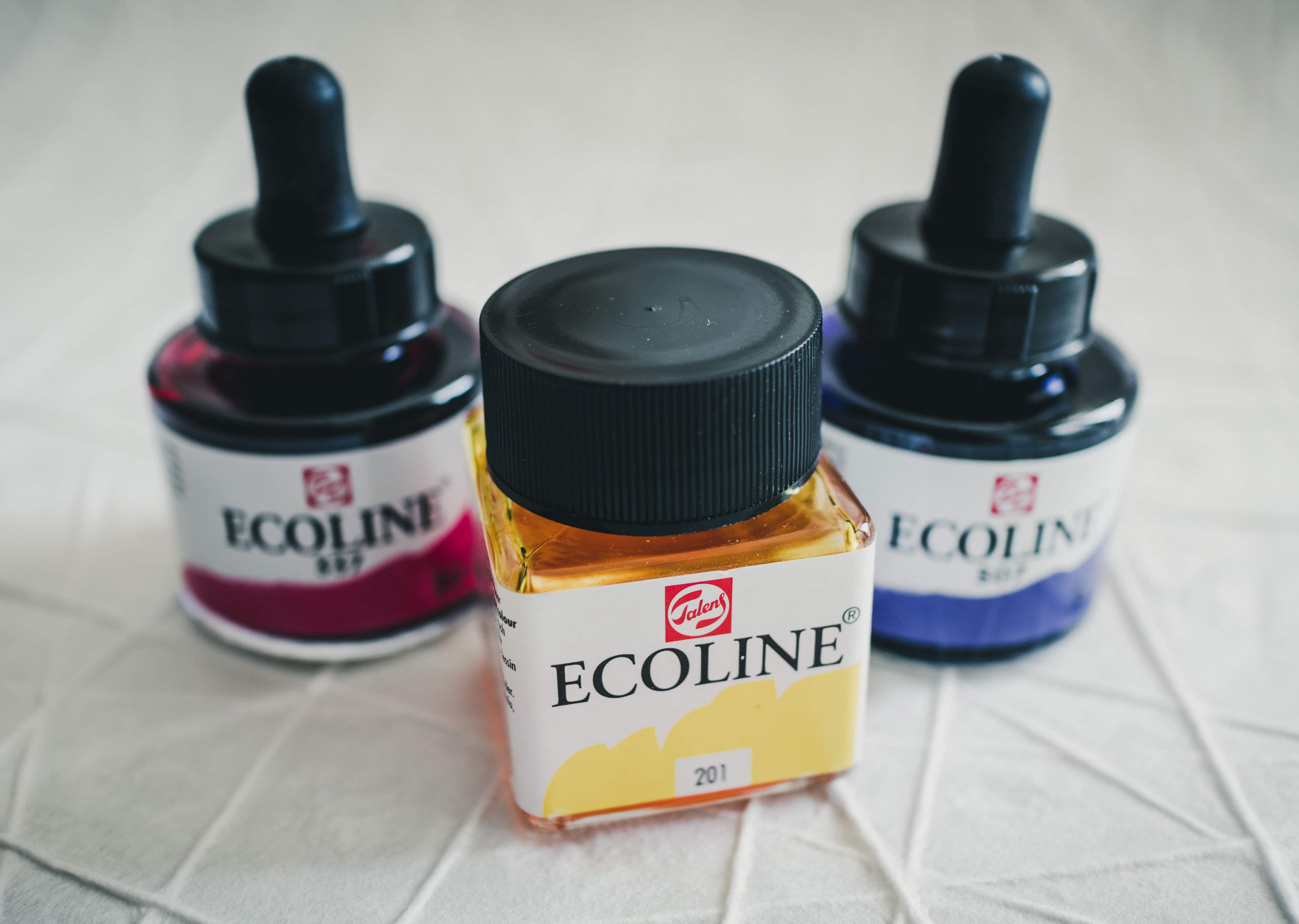 Ecoline-watercolor-ink-bottles-red-blue-yellow Closeup of red, blue, and yellow Ecoline watercolor ink bottles sitting on a table
