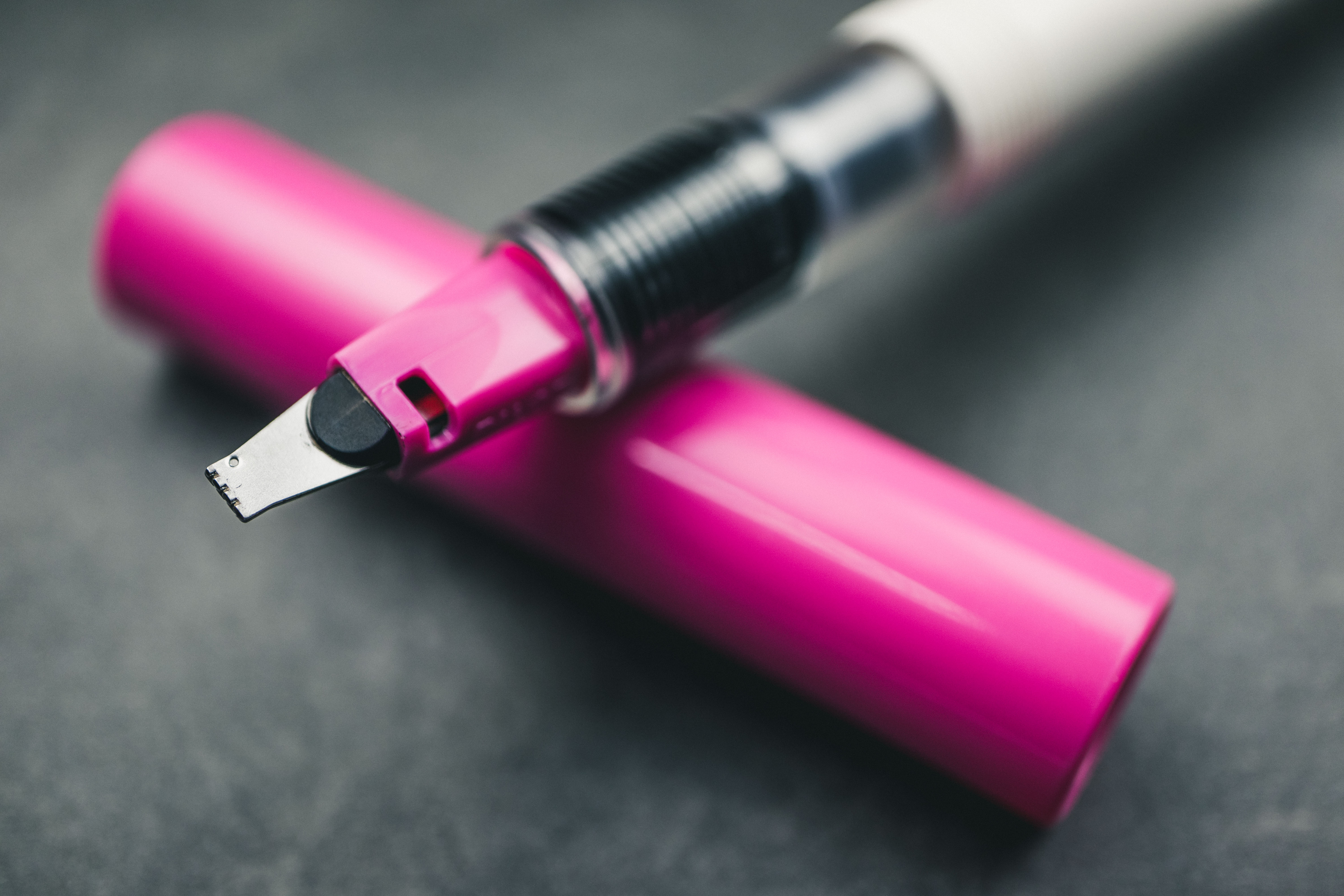 3mm-Pink-Pilot-Parallel-pen-nib-closeup Super closeup of pink 3mm Pilot Parallel pen nib and pen section resting on pen cap and a gey granite surface